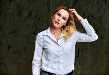 Beyaz tişörtlü, gri arka planda uçan saçlı, gülümseyen sarışın bir kadının portresi. Hem de kameranın önünde..