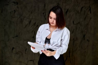 Gri arka planda beyaz gömlekli, güzel, gülümseyen esmer, beyaz bir kız öğrencinin portresi. Farklı pozlarda kameranın önünde durmak..