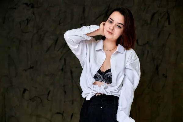 Porträt einer hübsch lächelnden brünetten kaukasischen Studentin in weißem Hemd auf grauem Hintergrund. in verschiedenen Posen direkt vor der Kamera stehen. — Stockfoto