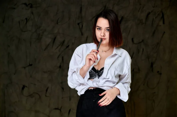 Retrato de una guapa morena sonriente estudiante caucásica con una camisa blanca sobre un fondo gris. De pie justo en frente de la cámara en varias poses . — Foto de Stock