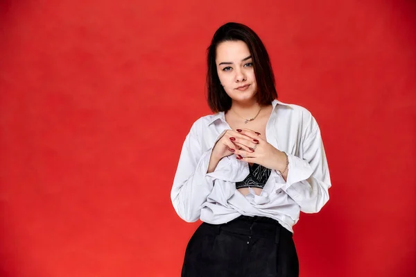 Portrait of a pretty smiling brunette Caucasian female student girl in a white shirt on a red background. Standing right in front of the camera in various poses. — Stock Photo, Image