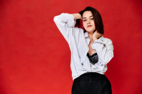 Retrato de una guapa morena sonriente estudiante caucásica con una camisa blanca sobre un fondo rojo. De pie justo en frente de la cámara en varias poses . — Foto de Stock