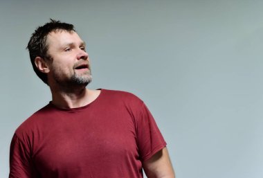 Gri arka planda bordo bir tişörtle 40 yıllık vahşi, tıraşsız, orta yaşlı bir adamın portresi. Kameranın önünde duruyor, konuşuyor, duygularını gösteriyor. Ellerini sallıyor..