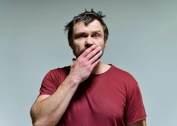 Retrato de um selvagem despenteado homem de meia-idade sem barba de 40 anos em uma camiseta borgonha em um fundo cinza. Ele fica mesmo em frente à câmara, a falar, a mostrar emoções. Acena com as mãos . — Fotografia de Stock