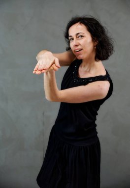 Model, canlı duygularla kameranın önünde duruyor. Gri arka planda siyah elbiseli, tatlı, gülümseyen esmer bir kadının dikey portresi..