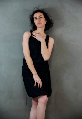 Model, canlı duygularla kameranın önünde duruyor. Gri arka planda siyah elbiseli, tatlı, gülümseyen esmer bir kadının dikey portresi..