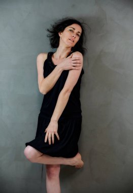 Model, canlı duygularla kameranın önünde duruyor. Gri arka planda siyah elbiseli, tatlı, gülümseyen esmer bir kadının dikey portresi..