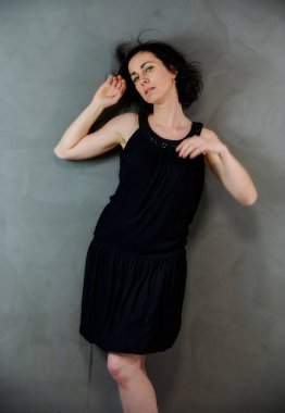 Model, canlı duygularla kameranın önünde duruyor. Gri arka planda siyah elbiseli, tatlı, gülümseyen esmer bir kadının dikey portresi..