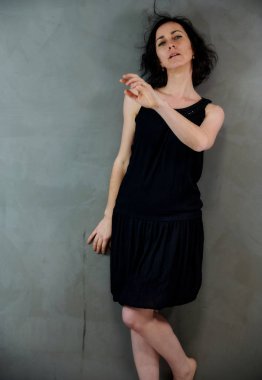 Model, canlı duygularla kameranın önünde duruyor. Gri arka planda siyah elbiseli, tatlı, gülümseyen esmer bir kadının dikey portresi..