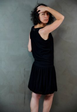 Model, canlı duygularla kameranın önünde duruyor. Gri arka planda siyah elbiseli, tatlı, gülümseyen esmer bir kadının dikey portresi..