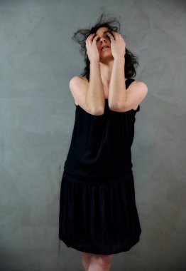 Model, canlı duygularla kameranın önünde duruyor. Gri arka planda siyah elbiseli, tatlı, gülümseyen esmer bir kadının dikey portresi..