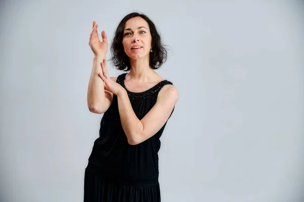 Portrait d'une jolie femme brune en robe noire sur fond blanc. Affiche des émotions avec les mains dans différentes poses juste en face de la caméra . — Photo