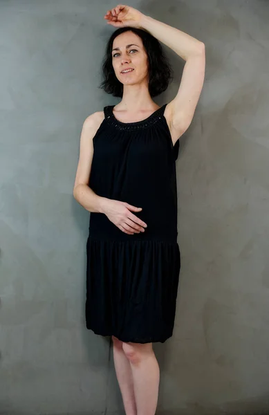 Portrait pleine longueur d'une jolie femme brune émotionnelle en robe noire sur fond gris alternatif à l'intérieur vintage. Debout devant la caméra . — Photo