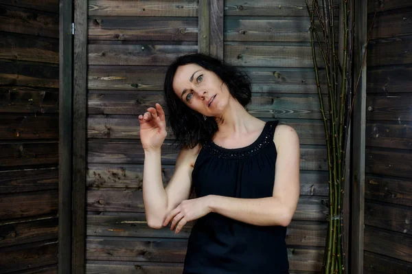 Retrato de una guapa morena sonriente en vestido negro sobre fondo de madera en interior vintage. De pie justo en frente de la cámara con emociones vívidas . — Foto de Stock