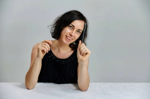 Portrait d'une jolie femme brune souriante parlant dans une robe noire sur un fond blanc. Assis à une table juste en face de la caméra avec des émotions vives . — Photo