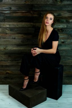 The concept of glamor, style. The model sits in different poses on an alternative stand in front of the camera. Portrait of a pretty blonde girl with long hair and great makeup on a wooden background.