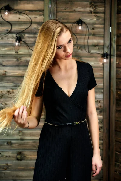 Het concept van glamour, stijl. Verticaal portret van een mooi blond meisje met lang haar en uitstekende make-up op een houten achtergrond met verlichting. Staande in verschillende houdingen voor de camera. — Stockfoto