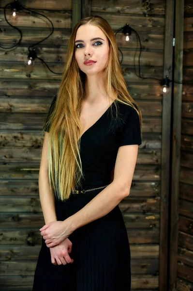 O conceito de glamour, estilo. Retrato vertical de uma linda menina loira com cabelos longos e excelente maquiagem em um fundo de madeira com luzes. Em pé em diferentes poses na frente da câmera . — Fotografia de Stock