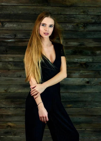 The concept of glamor, style. Model Stands in different poses in front of the camera. Vertical portrait of a pretty blonde girl with long hair and great makeup on a wooden background. — Stockfoto