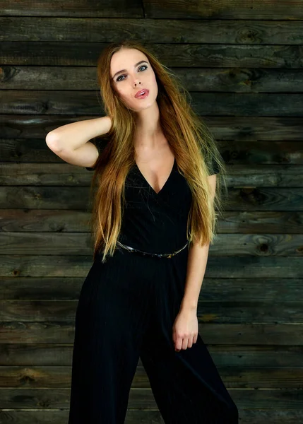 The concept of glamor, style. Model Stands in different poses in front of the camera. Vertical portrait of a pretty blonde girl with long hair and great makeup on a wooden background. — Stok fotoğraf