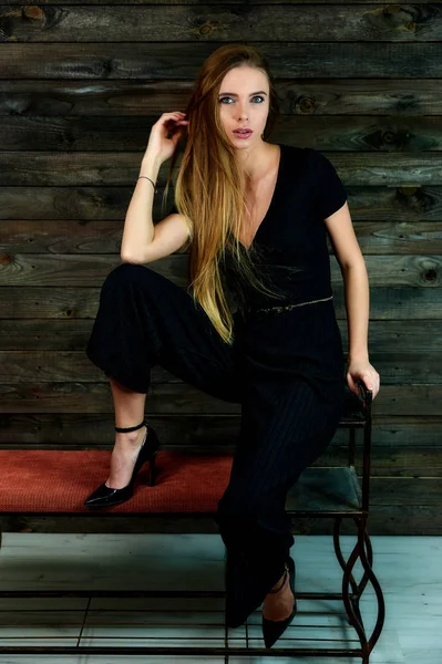 The model sits in various poses in front of the camera on a stand. The concept of fashion and style. Portrait of a pretty blonde girl with long hair and great makeup on a wooden background. — Stock Photo, Image