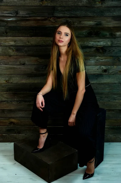 Het concept van glamour, stijl. Het model zit in verschillende poses op een alternatieve stand voor de camera. Portret van een mooi blond meisje met lang haar en geweldige make-up op een houten achtergrond. — Stockfoto