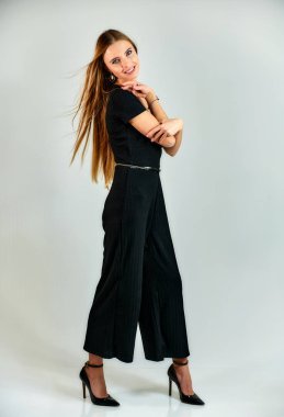 Full-length portrait of a pretty blonde girl with long hair and excellent make-up on a white background. Model student manager stands in different poses in front of the camera in the studio.
