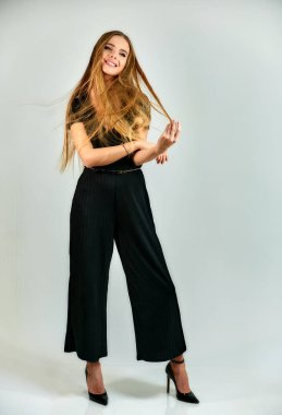 Full-length portrait of a pretty blonde girl with long hair and excellent make-up on a white background. Model student manager stands in different poses in front of the camera in the studio.