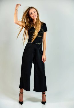 The concept of fashion and style. The model stands in different poses in front of the camera. Full-length portrait of a pretty blonde girl with long hair and excellent make-up on a white background.