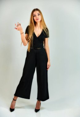 The model stands in different poses in front of the camera. The concept of fashion and style. Full-length portrait of a pretty blonde girl with long hair and excellent make-up on a white background.