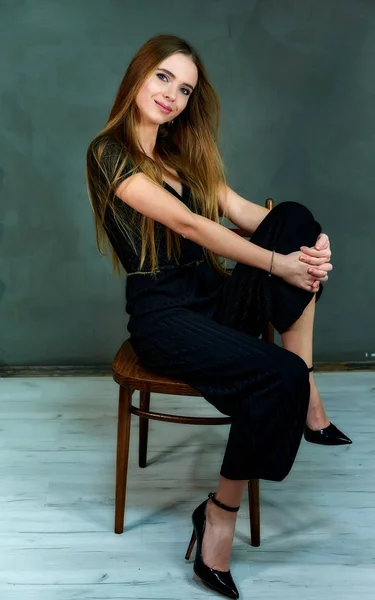 Το μοντέλο κάθεται σε διαφορετικές στάσεις σε μια καρέκλα μπροστά από την κάμερα. Η έννοια της αίγλης, στυλ. Πορτρέτο ενός όμορφου ξανθού κοριτσιού με μακριά μαλλιά και εξαιρετικό μακιγιάζ σε γκρι φόντο. — Φωτογραφία Αρχείου