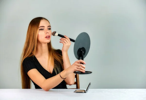 The model sits in different poses at the table and does makeup in front of the camera. Portrait of a pretty blonde girl with long hair and great makeup on a white background. — Stockfoto