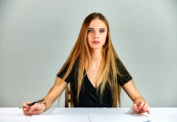 Ritratto di una bella ragazza bionda con i capelli lunghi e grande trucco su uno sfondo bianco. Modello studente manager seduto in pose diverse a un tavolo di fronte alla telecamera in studio . — Foto Stock