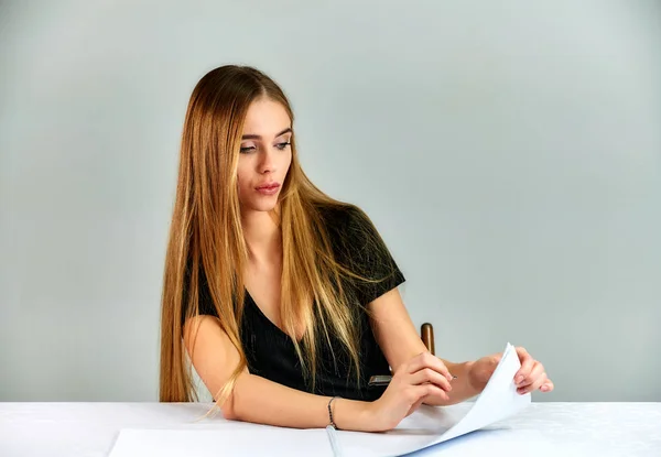 Ritratto di una bella ragazza bionda con i capelli lunghi e grande trucco su uno sfondo bianco. Modello studente manager seduto in pose diverse a un tavolo di fronte alla telecamera in studio . — Foto Stock