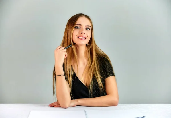 Portrait of a pretty blonde girl with long hair and great makeup on a white background. Model student manager sitting in different poses at a table in front of the camera in the studio. — Stockfoto