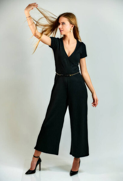 The concept of fashion and style. The model stands in different poses in front of the camera. Full-length portrait of a pretty blonde girl with long hair and excellent make-up on a white background.