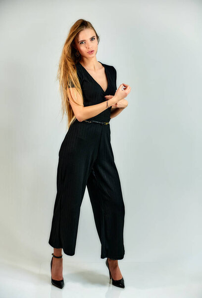 The concept of fashion and style. The model stands in different poses in front of the camera. Full-length portrait of a pretty blonde girl with long hair and excellent make-up on a white background.