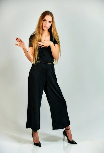 The model stands in different poses in front of the camera. The concept of fashion and style. Full-length portrait of a pretty blonde girl with long hair and excellent make-up on a white background.