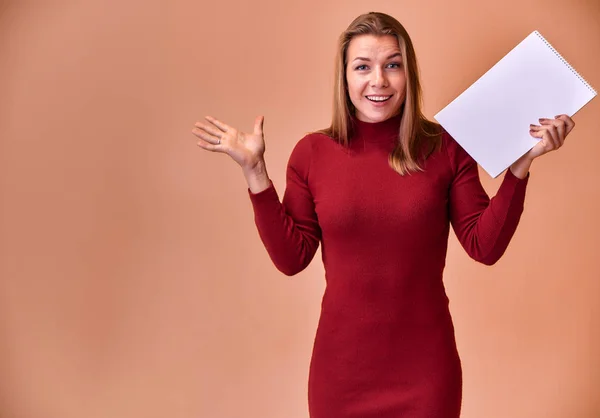 Ritratto di una bella ragazza bionda con un bel sorriso e denti eccellenti in un abito bordeaux con una cartella tra le mani su uno sfondo rosa. Carino guarda la fotocamera, in piedi dritto . — Foto Stock