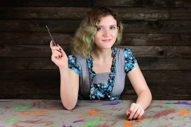 Turkuaz süveter giyen sevimli genç bir kadının yatay fotoğraf konsepti. Güzel kıvırcık saçlı güzel bir kızın portresi süslü bir masada, tahta bir arka planda oturuyor..