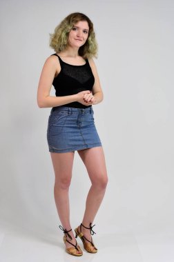 Siyah tişörtlü ve mavi etekli genç bir kadının yatay fotoğraf konsepti beyaz arka planda kameranın önünde duruyor. Güzel kıvırcık saçlı güzel bir kızın tam boy portresi..