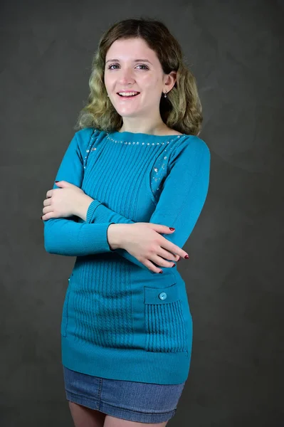 Portrait d'une jolie étudiante aux beaux cheveux bouclés se tient devant la caméra sur un fond gris. Concept photo verticale d'une jeune femme avec des émotions dans une robe bleue . — Photo