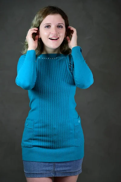 Retrato de uma menina estudante bonita com cabelo encaracolado bonito está de pé na frente da câmera em um fundo cinza. Conceito foto vertical de uma jovem com emoções em um vestido azul . — Fotografia de Stock