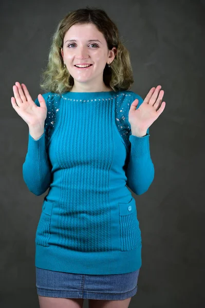Egy gyönyörű, göndör hajú diáklány portréja áll a kamera előtt, szürke háttérrel. Koncepció függőleges fotó egy fiatal nő érzelmekkel egy kék ruha. — Stock Fotó