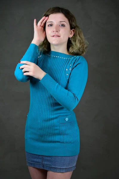 Portrait d'une jolie étudiante aux beaux cheveux bouclés se tient devant la caméra sur un fond gris. Concept photo verticale d'une jeune femme avec des émotions dans une robe bleue . — Photo