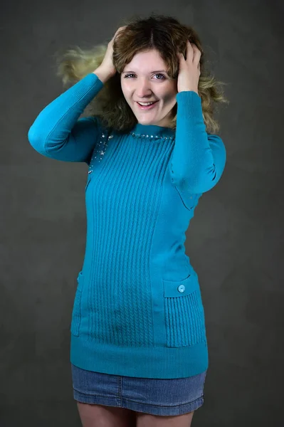 Concetto foto verticale di una giovane donna con emozioni in un abito blu. Ritratto di una bella studentessa con bei capelli ricci è in piedi davanti alla fotocamera su uno sfondo grigio . — Foto Stock