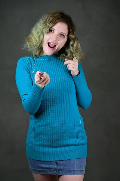 Conceito foto vertical de uma jovem com emoções em um vestido azul. Retrato de uma menina estudante bonita com cabelo encaracolado bonito está de pé na frente da câmera em um fundo cinza . — Fotografia de Stock