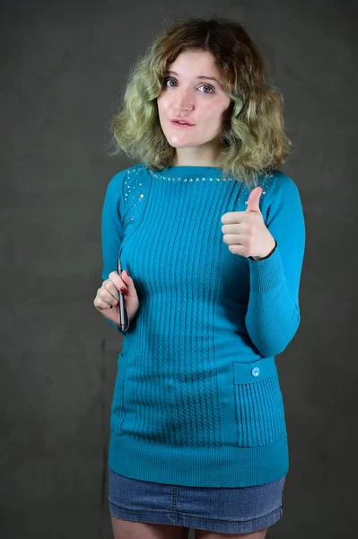 Begreppet vertikalt foto av en ung kvinna med känslor i en blå klänning. Porträtt av en söt student flicka med vackra lockigt hår står framför kameran på en grå bakgrund. — Stockfoto