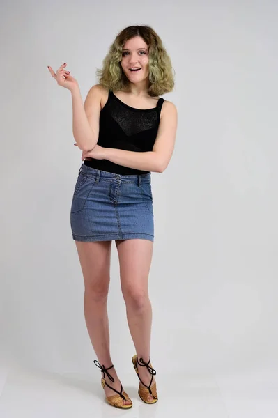 白地には黒いTシャツと青いスカートを着た若い女性の横写真のコンセプトがカメラの前に立っている。フル長いですポルノの美しいです巻き毛のある女の子. — ストック写真