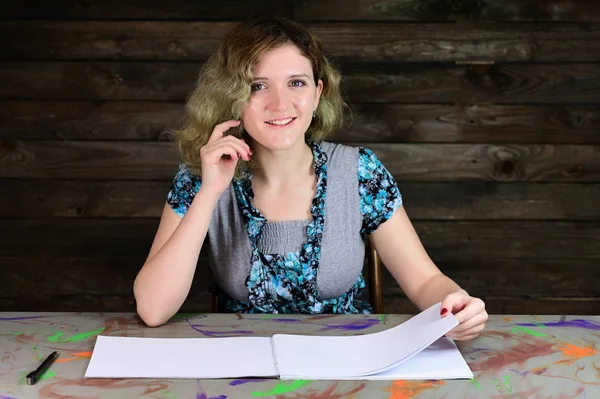 Horizontaal foto concept van een leuke jonge vrouw met een map in een turquoise trui. Portret van een mooi student meisje met mooi krullend haar zittend aan een versierde tafel op een houten achtergrond. Rechtenvrije Stockafbeeldingen